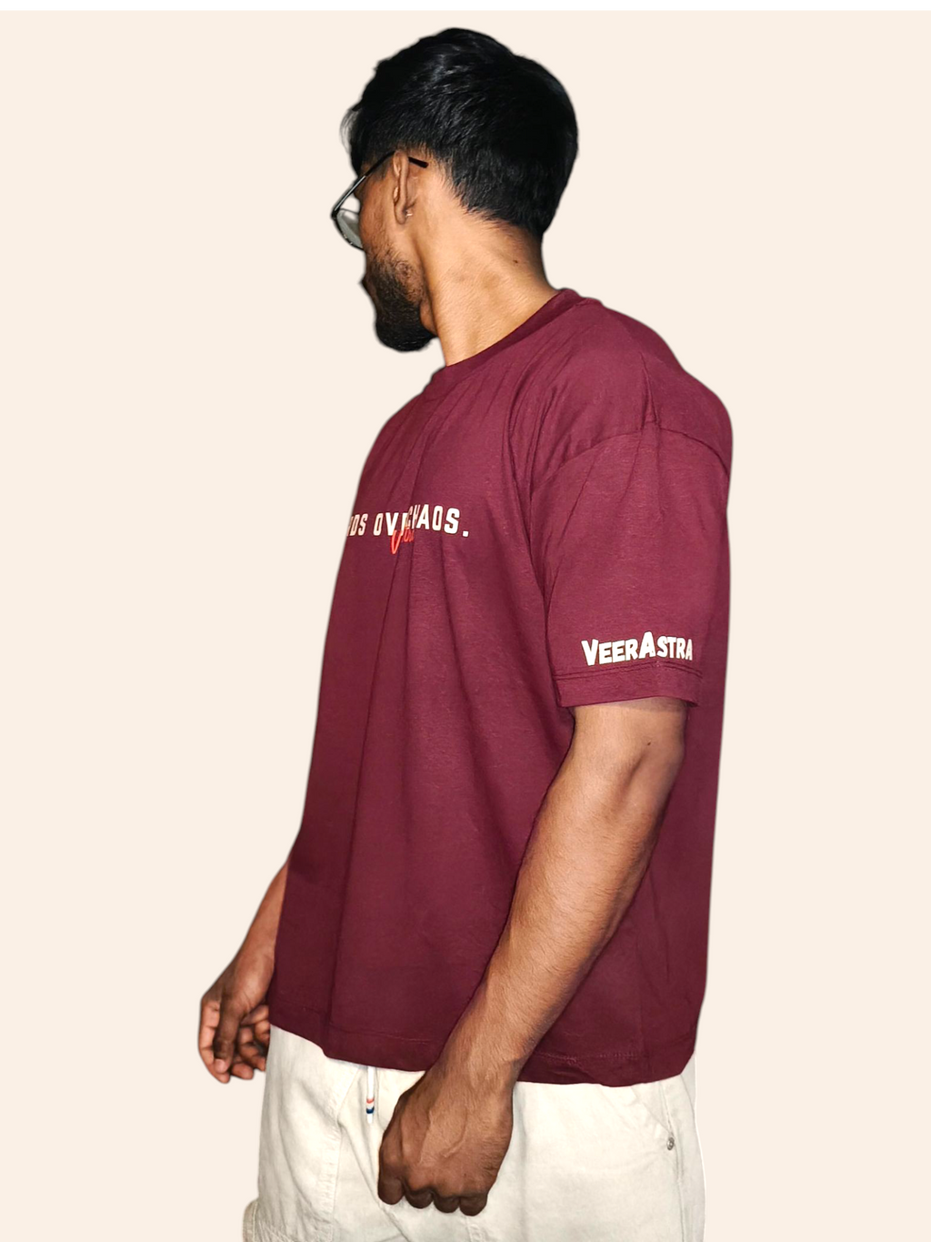 Man wearing a VeerAstra maroon t-shirt with branding on a beige background