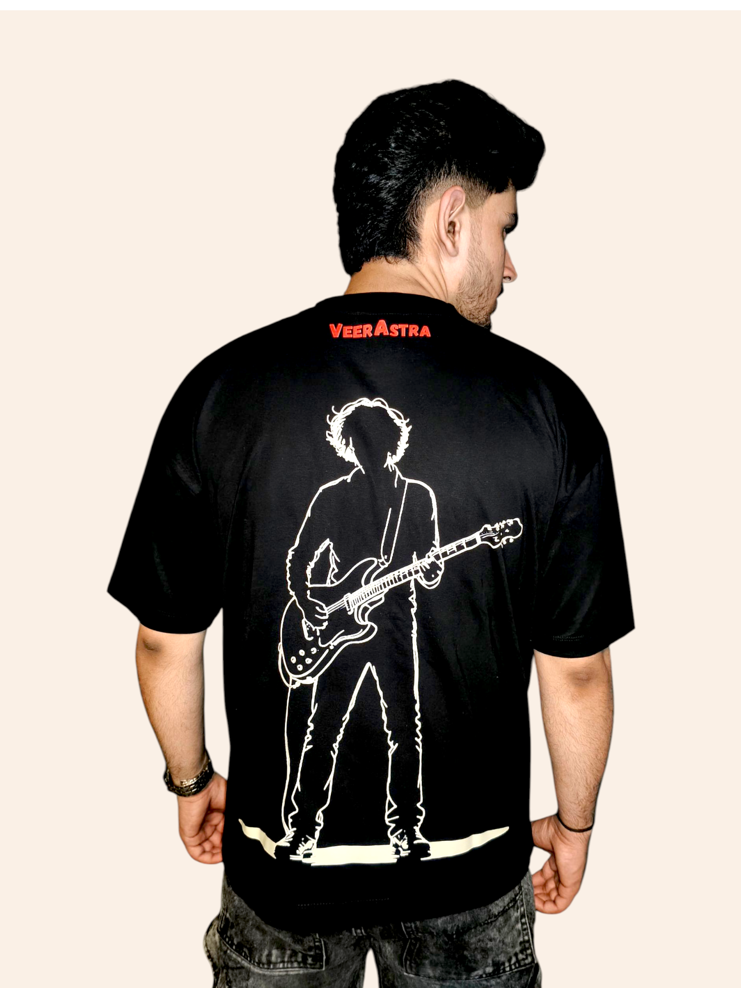 Person wearing a VeerAstra black t-shirt with a graphic design on the back, standing against a beige background.