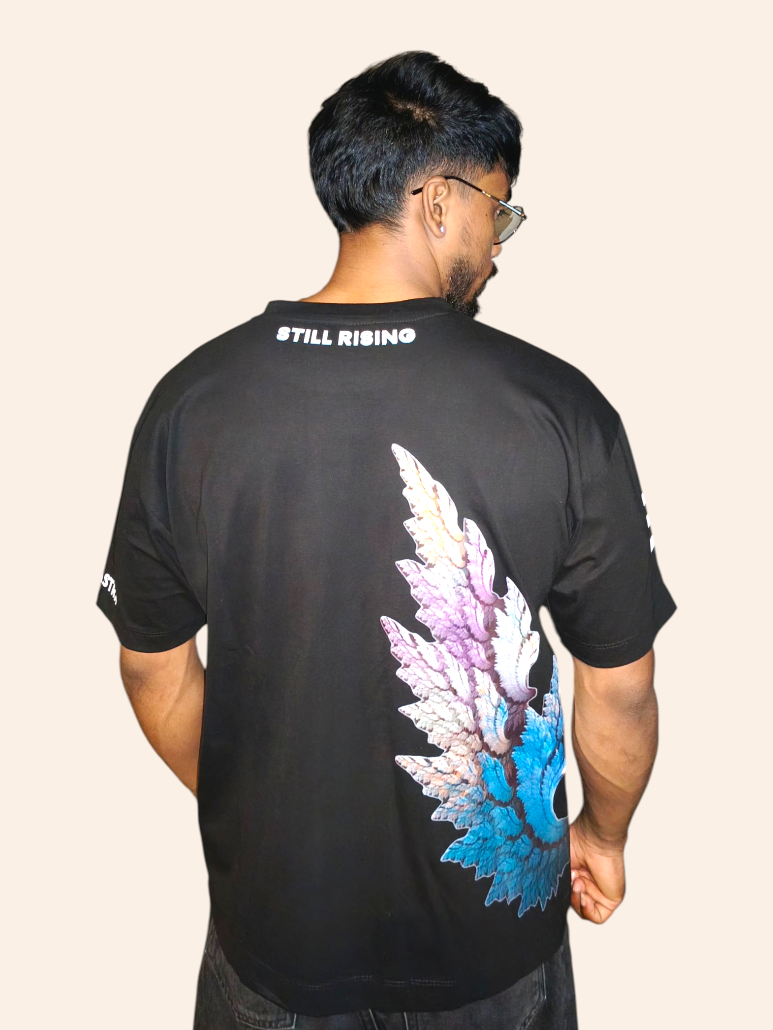 Man wearing a black VeerAstra t-shirt with colorful design on the back and 'STILL RISING' text.