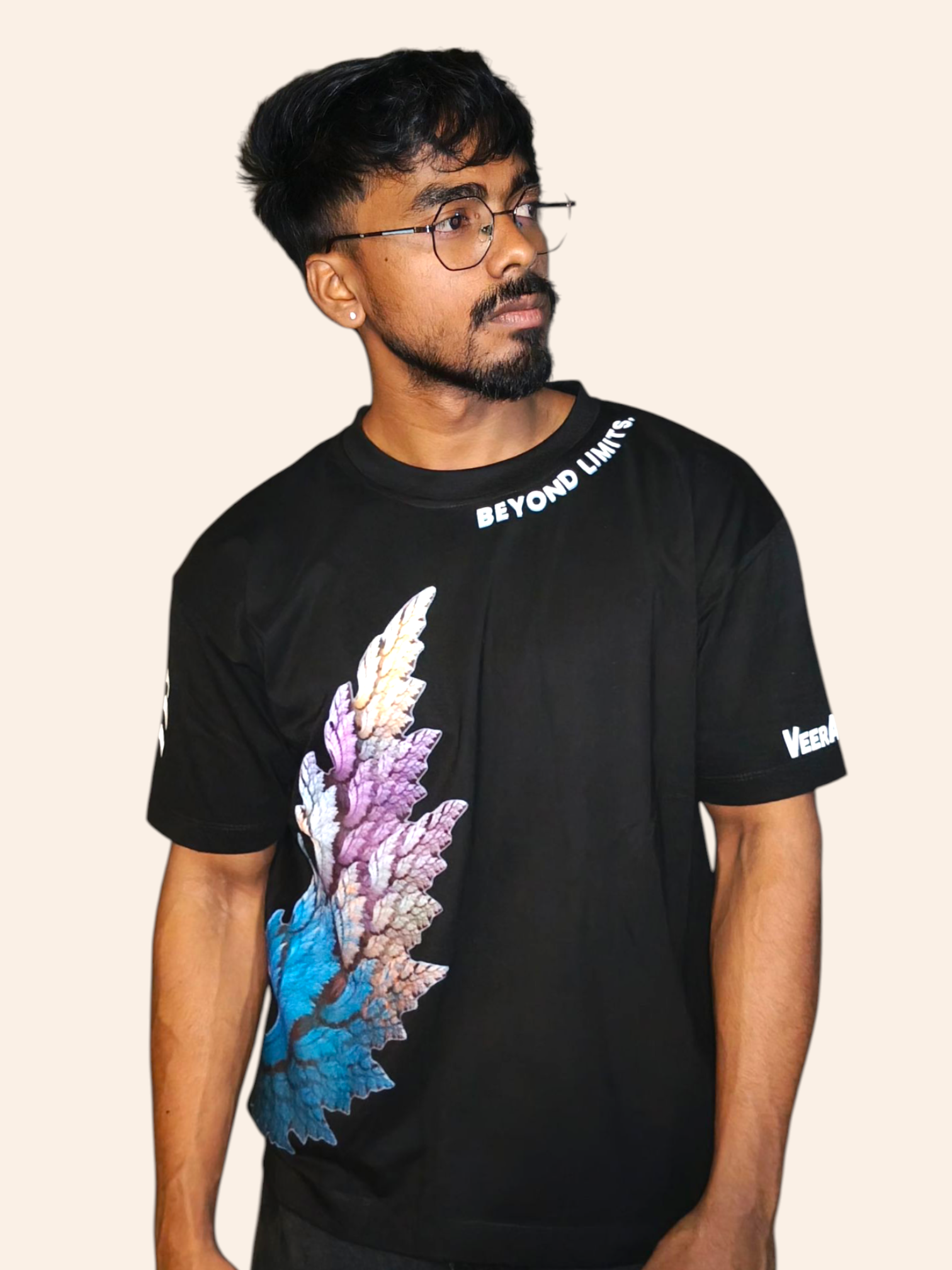 Man wearing a black VeerAstra t-shirt with colorful leaf design and 'Beyond Limits' text on a beige background