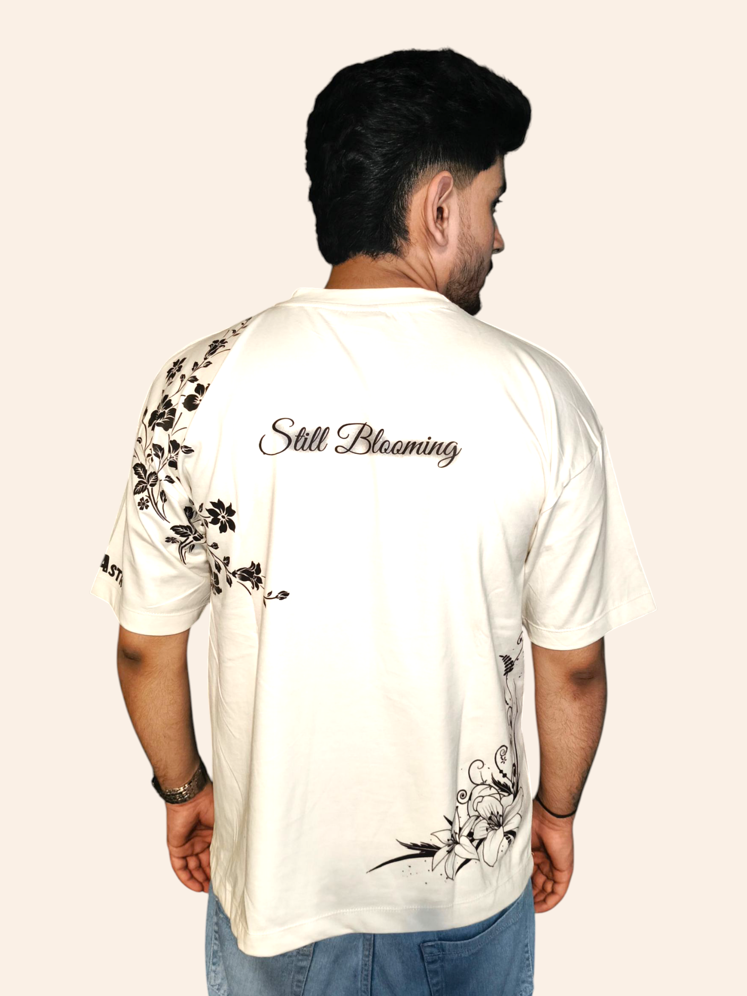 Man wearing a VeerAstra white t-shirt with floral designs and 'Still Blooming' text on the back.